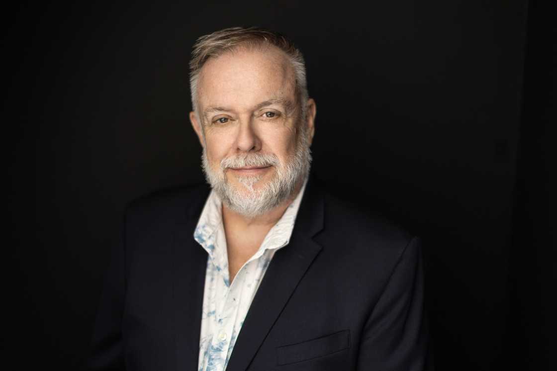 Patrick Raftery smiling and wearing a tan suit with a black shirt.