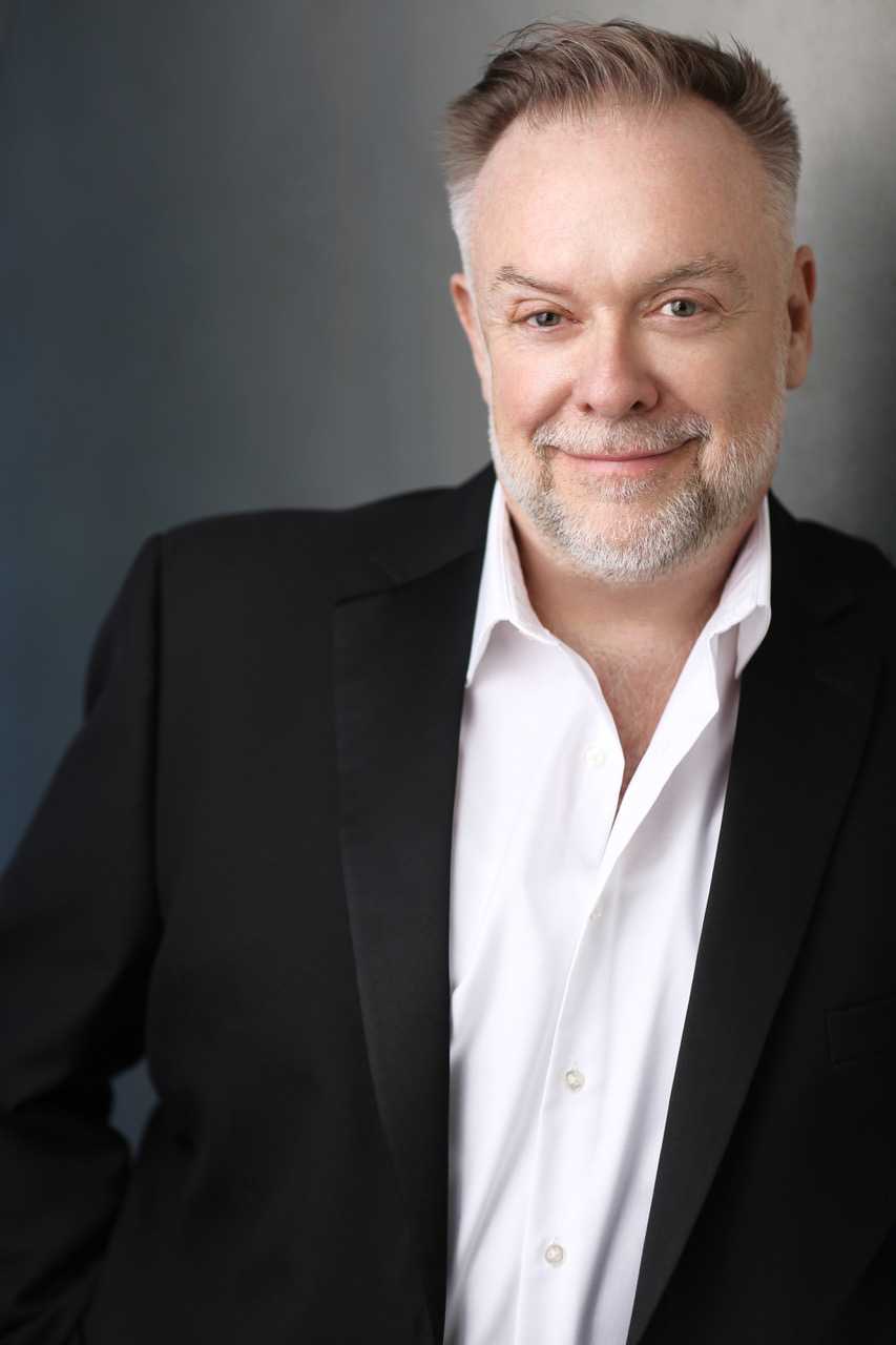 Patrick Raftery smiling and wearing a black suit with a white shirt.