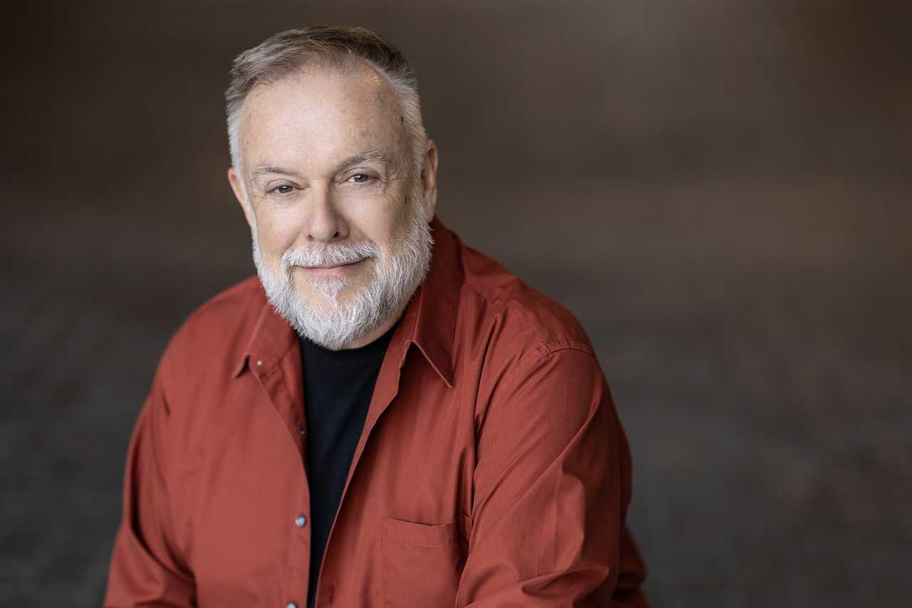 A headshot of Patrick Raftery wearing a red shirt in 2023.