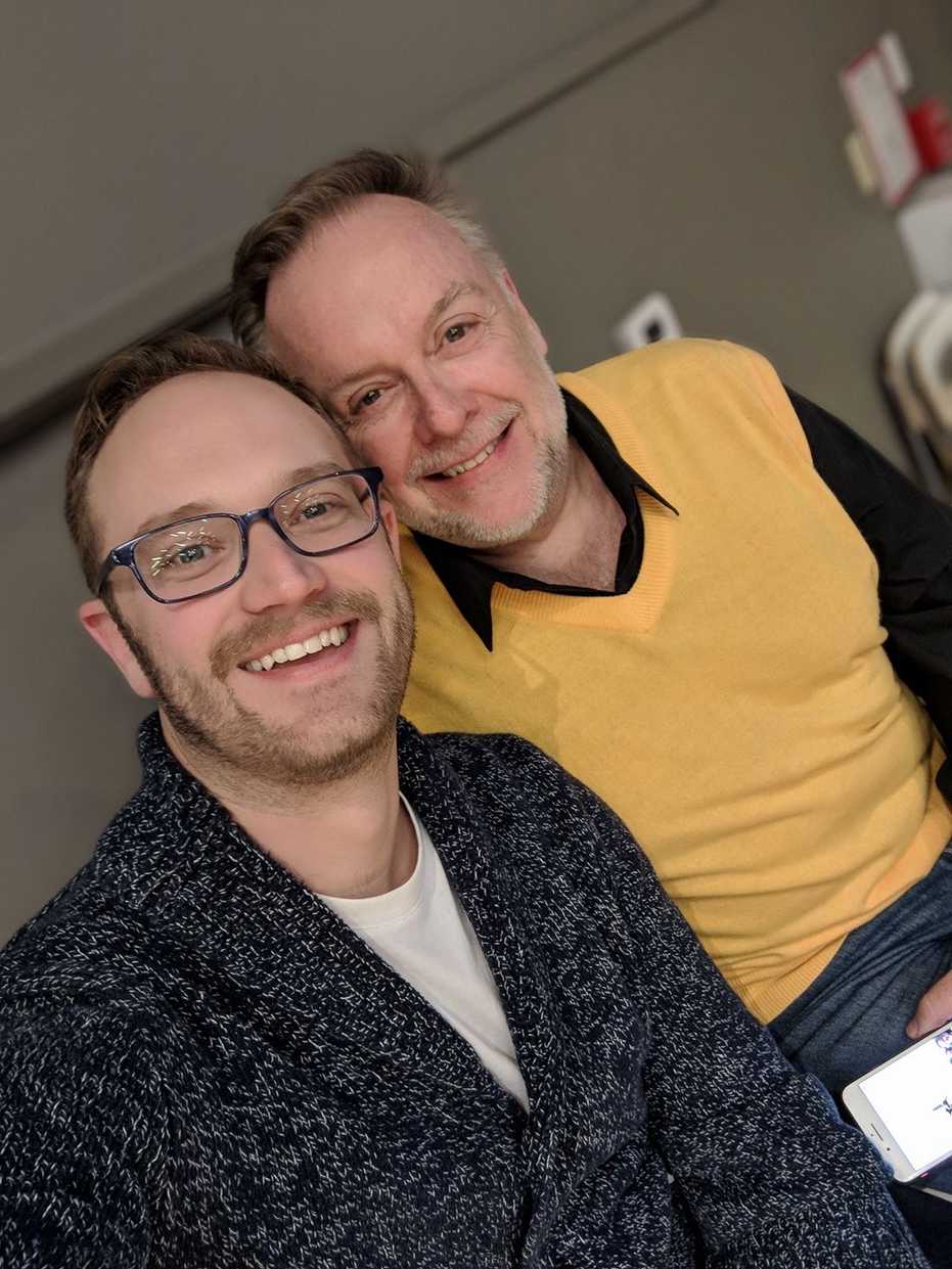 Patrick Raftery smiling while wearing a yellow sweater and sitting next to his voice student Andrew Love.